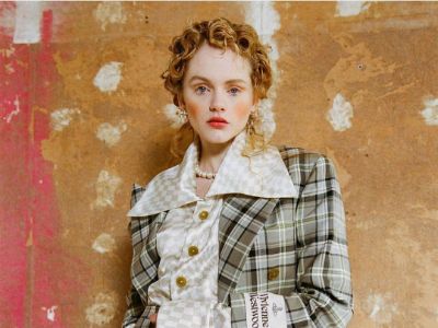 Emma Laird has curly short hair and is wearing a fancy jacket.